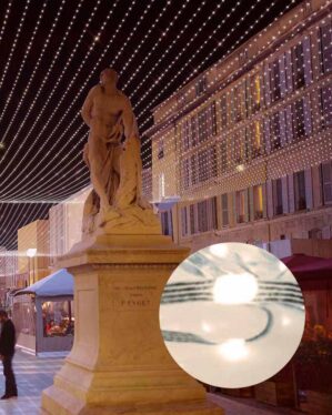 Gade dekoreret med et lysloft af varme hvide LED-lys, der strækker sig mellem bygninger og over en statue, hvilket skaber en festlig og indbydende atmosfære. Nærbillede viser en enkelt mikro LED-pære i lyskæden.