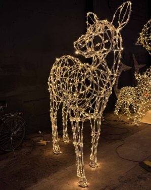 Stor hunhjortfigur i metalramme med varme LED-lys, opstillet i et mørkt rum. Kabler og lysfigurer ses i baggrunden, skaber stemning.