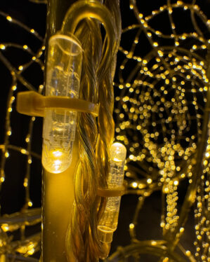 Detaljeret nærbillede af varm hvid LED integreret i en guld-pulverlakeret aluminiumsstruktur. LED-lyset er elegant fastgjort med klare kabler, hvilket sikrer en ren og poleret finish, der fremhæver den kunstneriske og funktionelle kvalitet af dekorationen.