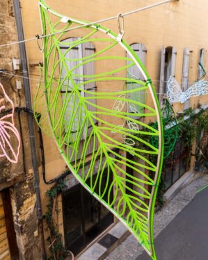 Sommer i en gade med store grønne plastikblade der hænger i wirer over gaden.