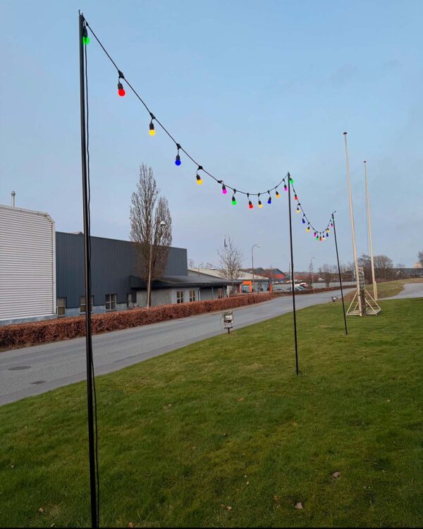 Sort aluminium stativ til lyskædeinstallation, monteret på en græsplæne. Designet til at holde lyskæder i spænd, skaber en elegant og funktionel belysningsløsning til udendørs dekoration.