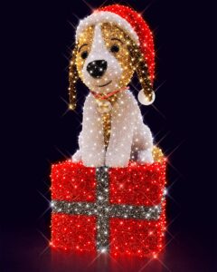 Stor LED-juledekoration af sød hund i nissehue med klokke om halsen, siddende på en lysende rød gaveæske med glitrende hvide og sølvfarvede detaljer.