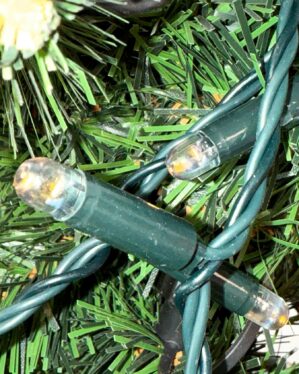 Nærbillede af grøn LED-lyskæde flettet ind i kunstigt juletræ. Pærerne har klar kapsel, grøn ledning og giver et varmt hvidt skær til dekorative opsætninger.