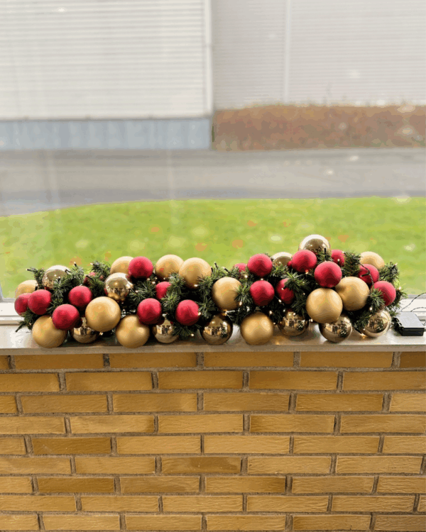 Færdigpyntet granguirlande med røde og champagne kugler samt varm hvide LED-lys. Skaber en klassisk, elegant og festlig julestemning i vindueskarmen.