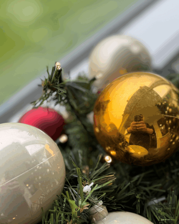 Nærbillede af granguirlande med røde, perlemor og guld julekugler samt varm hvide LED-lys. Fanger julens glans, refleksioner og hyggelige stemning i detaljen.