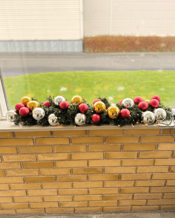 Pyntet granguirlande med røde, sølv- og guld kugler samt varm hvide LED-lys. Skaber en elegant og festlig julestemning i vindueskarmen.