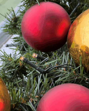 Detaljeret nærbillede af granguirlande med røde og guld julekugler samt varm hvide LED-lys. Viser tekstur, glød og klassisk julestemning i smuk balance.