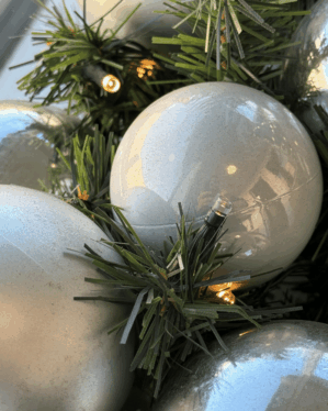 Nærbillede af juleguirlande med sølv og perlemor kugler og varm LED-belysning. De grønne grene og skinnende kugler skaber et elegant og vinterligt udtryk.