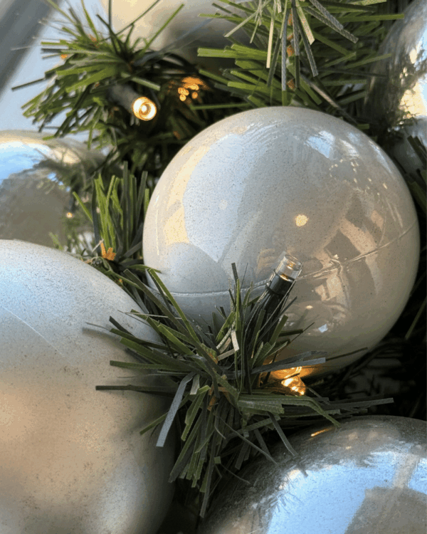 Nærbillede af juleguirlande med sølv og perlemor kugler og varm LED-belysning. De grønne grene og skinnende kugler skaber et elegant og vinterligt udtryk.