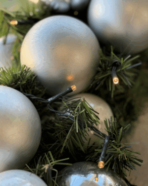 Detaljeret nærbillede af juleguirlande med sølv og perlemor kugler og varm LED-belysning. Skinnende kugler og grønne grene giver et elegant og moderne vinterudtryk.