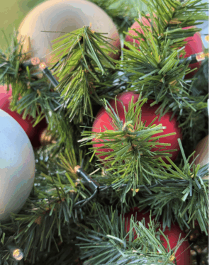 Detaljeret nærbillede af juleguirlande med grønne grene, røde, champagne og sølvfarvede kugler samt små varme LED-lys, der skaber en hyggelig og klassisk julestemning.