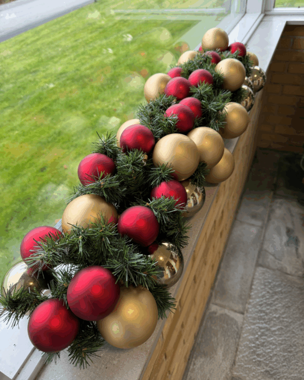 Elegant granguirlande pyntet med røde og champagne  julekugler, placeret i vindueskarm. Skaber et klassisk, varmt og festligt udtryk med harmonisk farvespil og julestemning.