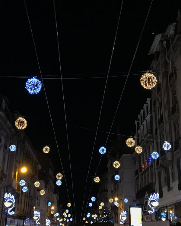Ophængte LED-lyskugler i kold og varm hvid lyser op over en bymidte om natten, skaber festlig stemning mellem bygninger og langs gaden med juleudsmykning.