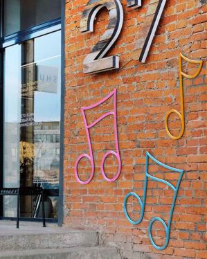 Farverige 2D-musiknode-motiver monteret på murstensfacade ved butik, skaber legende og kunstnerisk byudsmykning i offentligt byrum med fokus på kultur stemning design og visuel identitet.