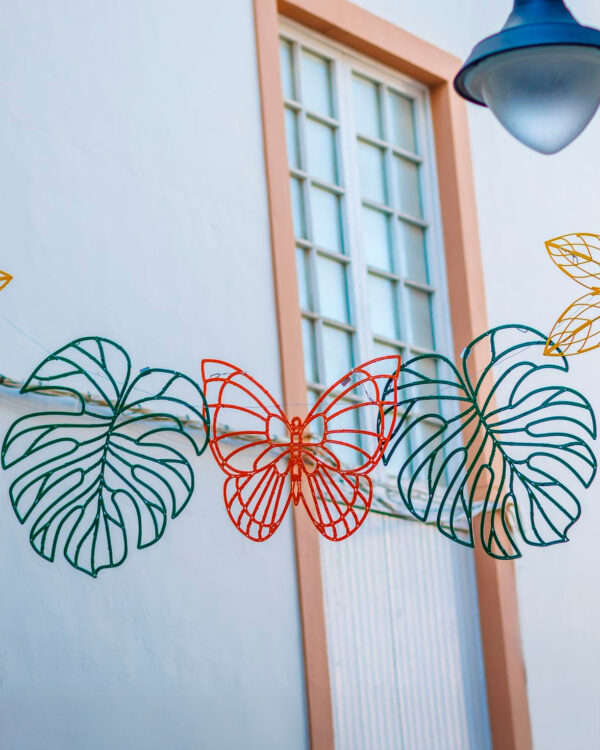 Dekorative 2D-blade med grønne blade og rød sommerfugl i bioprint, ophængt i wire, skaber farverig citydressing på facade i byrum og handelsgade sommerudsmykning professionelle miljøer