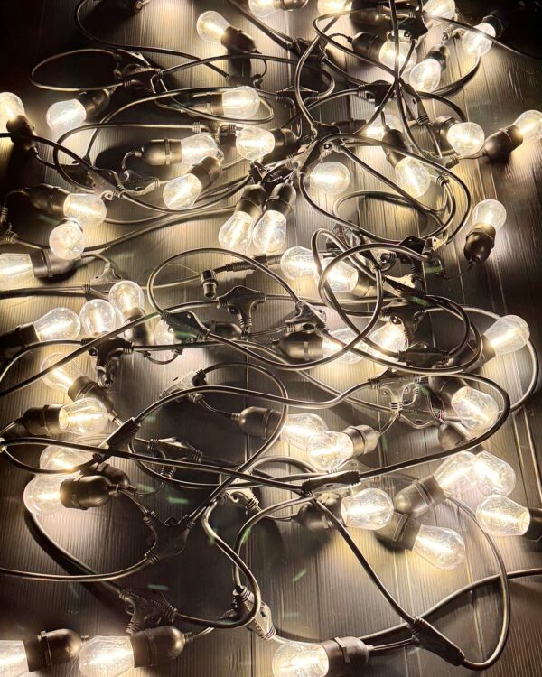 Sammenrullet sort party-lyskæde med E27-fatninger og varme LED-pærer, robust kabel og stik, velegnet til professionel indendørs og udendørs stemningsbelysning.