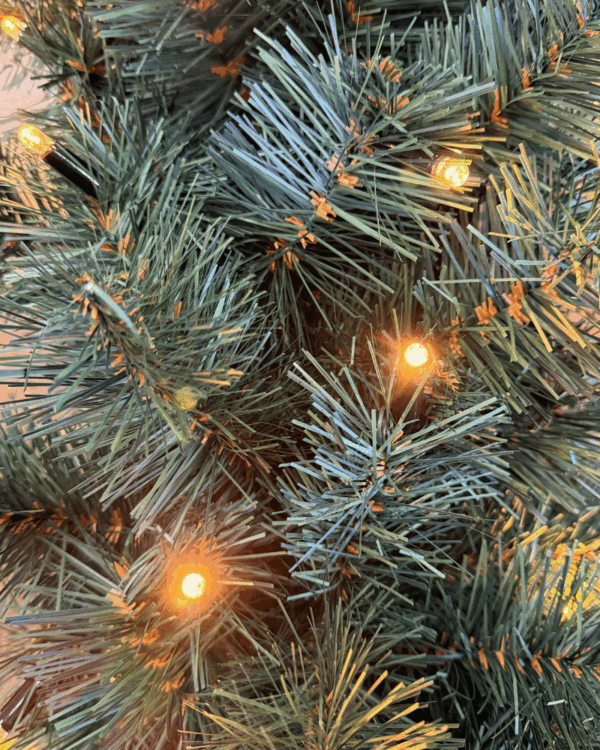 Nærbillede af kunstig granguirlande med tætte grønne nåle og integrerede varm hvide LED-lys, der skaber en hyggelig og stemningsfuld julebelysning til dekoration.
