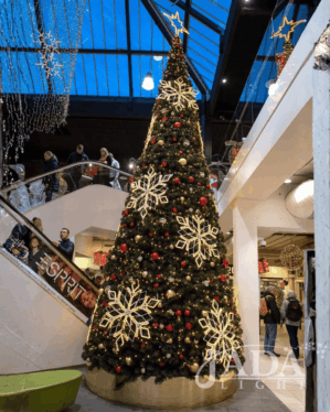 Stort juletræ i indendørs center med varm hvid 2D-topstjerne, snefnugsmotiver og røde kugler, skaber elegant og stemningsfuld juleudsmykning i det høje atrium.