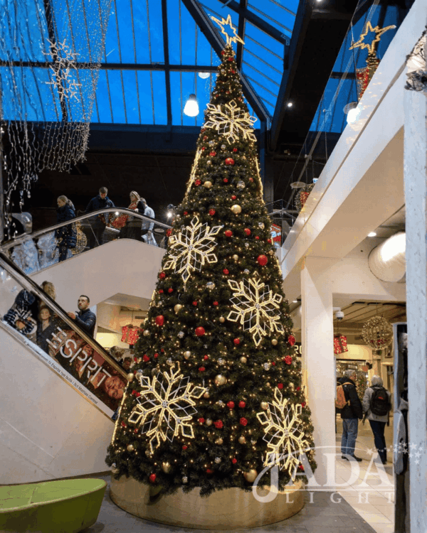 Stort juletræ i indendørs center med varm hvid 2D-topstjerne, snefnugsmotiver og røde kugler, skaber elegant og stemningsfuld juleudsmykning i det høje atrium.