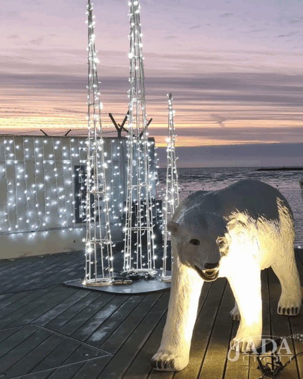 Kold hvide 3D-kegleformede lysdekorationer i forskellige højder, vist udendørs ved vandet sammen med oplyst isbjørn som stemningsfuld vinterudsmykning ved solnedgang.