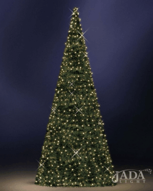 Højt kegleformet juletræ med tæt grøn carpet og varm hvid belysning, vist på mørk blå baggrund som elegant og stemningsfuld juleudsmykning.